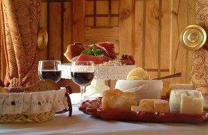 Tábua de queijos variados e enchidos com dois copos de vinho tinto, em ambiente rústico de madeira.