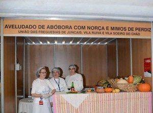 Três mulheres em estand de comida com abóboras e ingredientes, expositor para Festival de Sopas.
