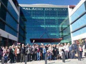 Grupo de pessoas reunidas em frente ao edifício Palácio do Gelo, com fachada de vidro azul.