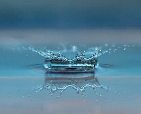 Coroa de água formada por respingo simétrico numa superfície líquida com fundo azul — ampliar imagem