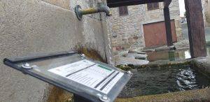 Tablet com formulário de análise junto a fontanário com água corrente em ambiente urbano medieval.