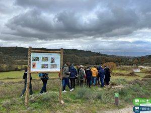 Grupo de alunos reunidos junto a painel educativo em paisagem montanhosa com nuvens.