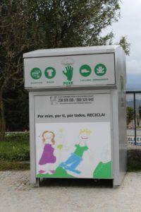 Contentor de recolha seletiva branco com cinco símbolos verdes indicando tipos de têxteis aceites e desenho infantil de duas crianças