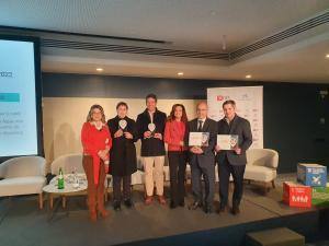 Seis pessoas em palco durante cerimónia de premiação, com trofeus e diplomas, logótipo BPI visível ao fundo.