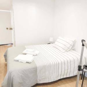 Quarto minimalista com cama de casal, roupa de cama branca com padrão de riscas, almofadas e mantas dobradas.