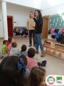 Dois adultos animam atividade com grupo de crianças sentadas no chão de uma sala de aula.