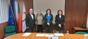 Quatro pessoas em pé junto a mesa de trabalho, com bandeiras de UE, Portugal e instituição ao fundo