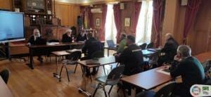 Sala de reunião com autoridades e bombeiros em torno de mesas com laptops e documentos, presidida por três elementos no estrado.