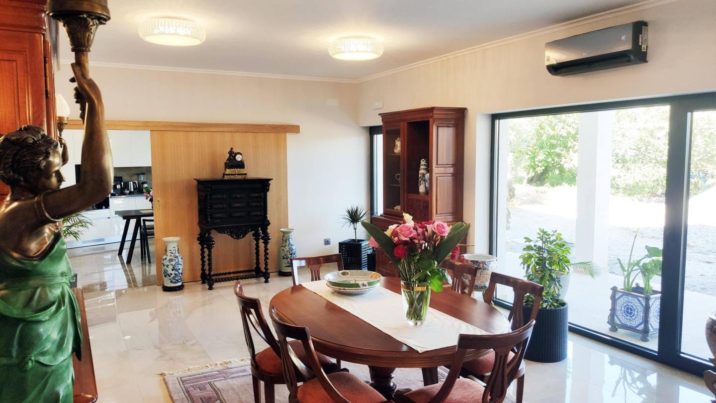 Sala com mesa de madeira, estátua grega, portas de vidro para jardim e flores frescas