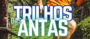 Corredor em trail running numa floresta verde com sobreposição de texto 'Trilhos das Antas'