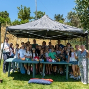 Grupo de crianças e adultos posados sob tenda cinzenta em espaço verde.