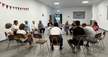 Grupo de pessoas sentadas em círculo durante sessão de informação em sala comunitária.