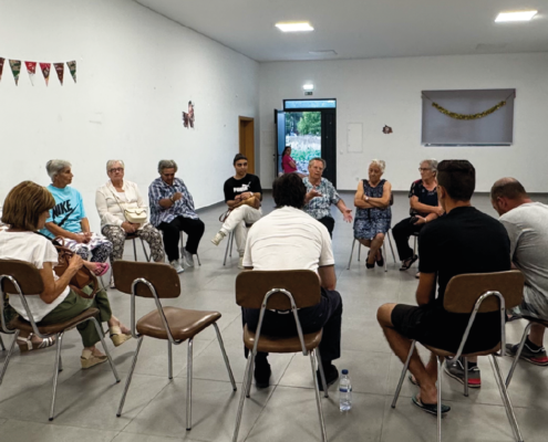 Grupo de pessoas sentadas em círculo durante sessão de informação em sala comunitária.